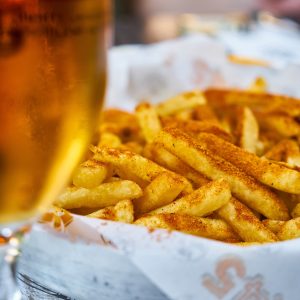 Glass of beer with a side of seasoned golden fries on a paper plater