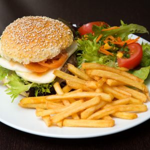 Lettuce, Tomatoe, Onion Cheese Hamburger with fries, including lettuce, tomatoes and shredded carrots on the side sitting on a white ceramic plate